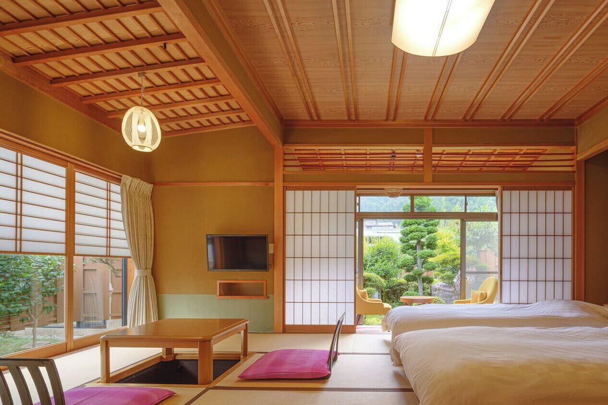 Ein traditioneller japanischer Raum mit Tatami-Boden, einem Bett, einem Fernseher und Blick ins Grüne.