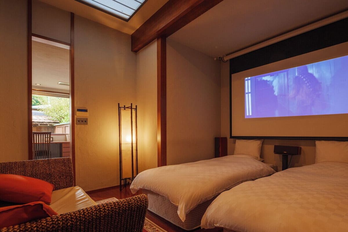 Ein Hotelzimmer mit zwei Betten, einer Projektionsleinwand und einer Sitzecke mit einem Sessel.