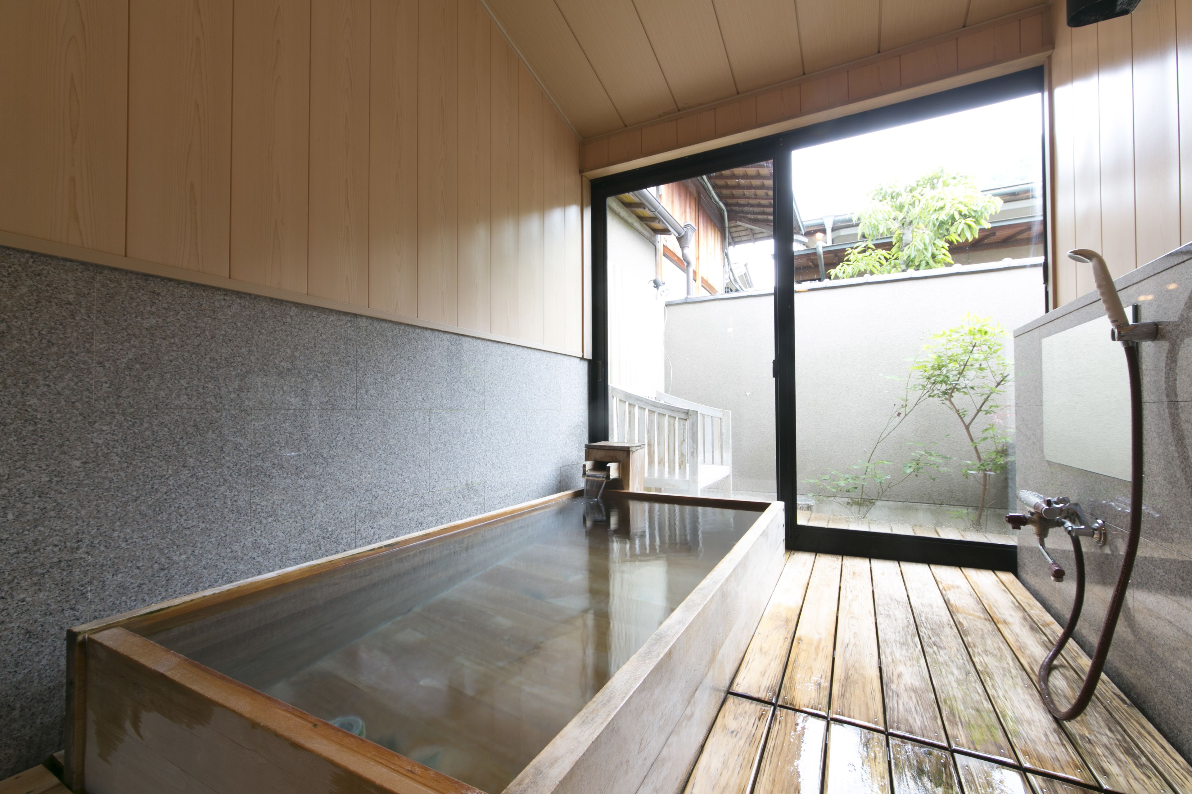 A traditional Japanese onsen with a wooden floor, a stone wall, and a glass-enclosed hot spring.