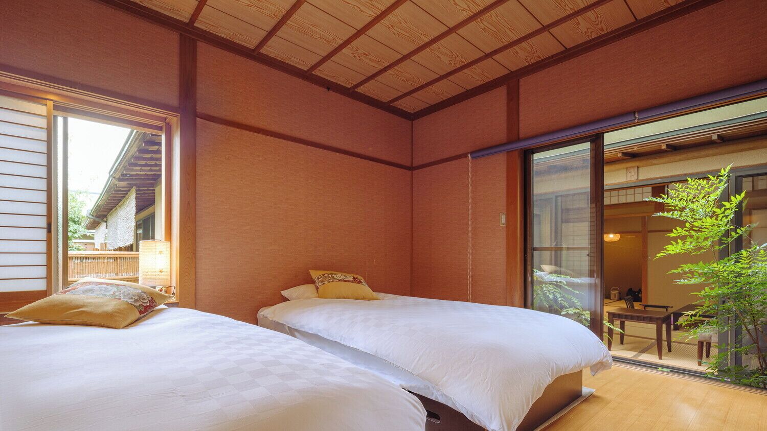 A traditional Japanese-style room with tatami flooring, two beds with white bedding, sliding doors, and a view of a traditional garden.
