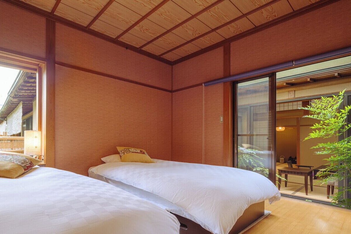 Ein traditioneller japanischer Raum mit Tatami-Boden, zwei Betten mit weißer Bettwäsche, Schiebetüren und Blick auf einen traditionellen Garten.