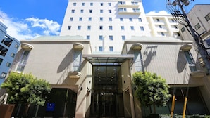 Entrada de un hotel con una cubierta de vidrio, un letrero que indica hotel y cielo despejado.