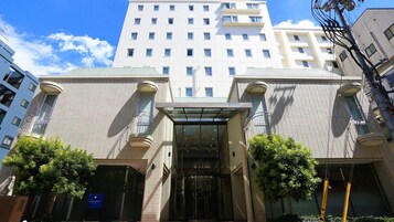 Entrada de un hotel con una cubierta de vidrio, un letrero que indica hotel y cielo despejado.
