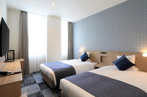 Habitación de hotel con dos camas, televisión, escritorio y ventana con cortinas.
