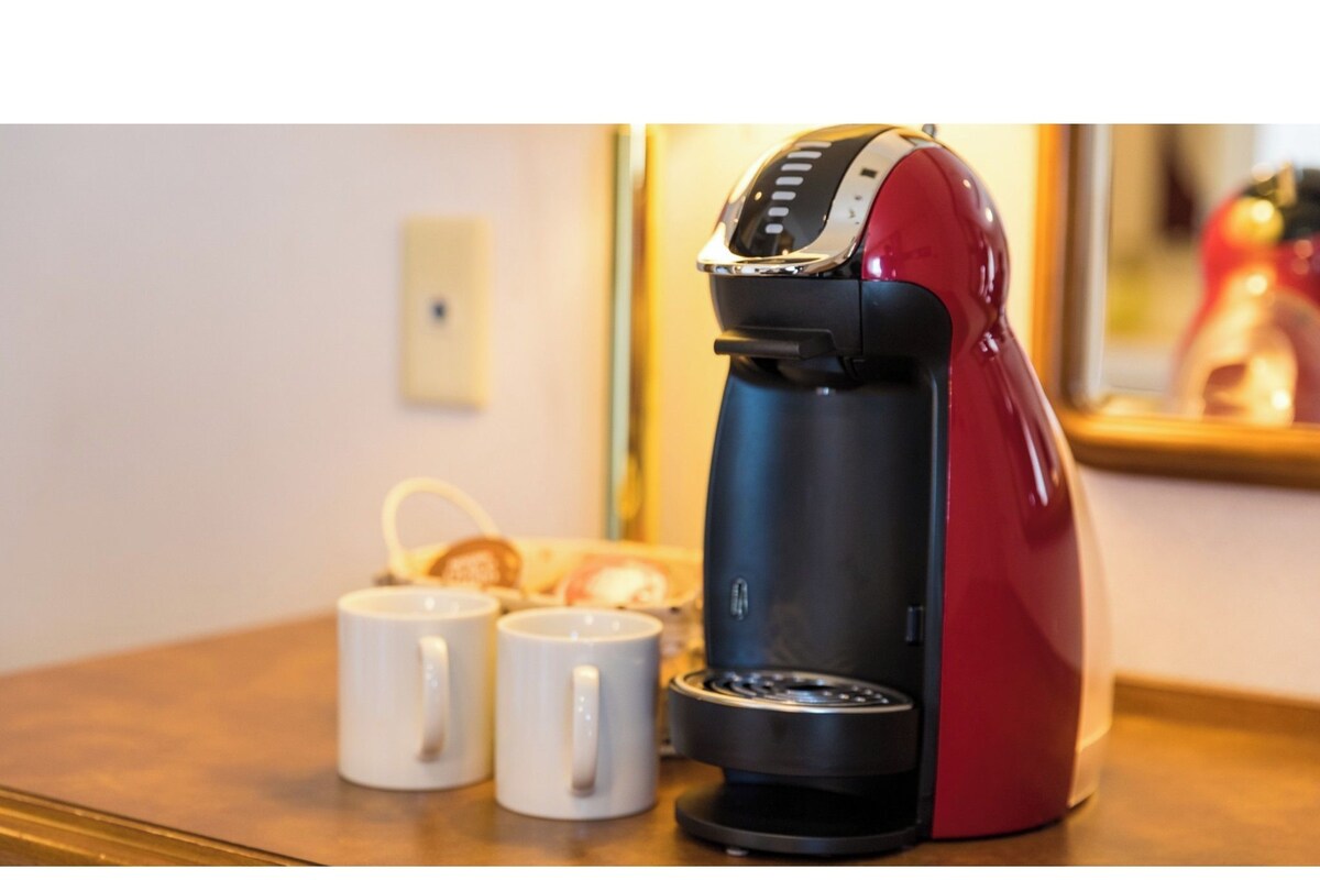 Una cafetera roja y negra sobre una mesa, con dos tazas blancas a su lado.