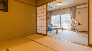 A traditional Japanese room with tatami flooring, a sliding shoji screen, a sofa, a telescope, and a view of mountains through large windows.