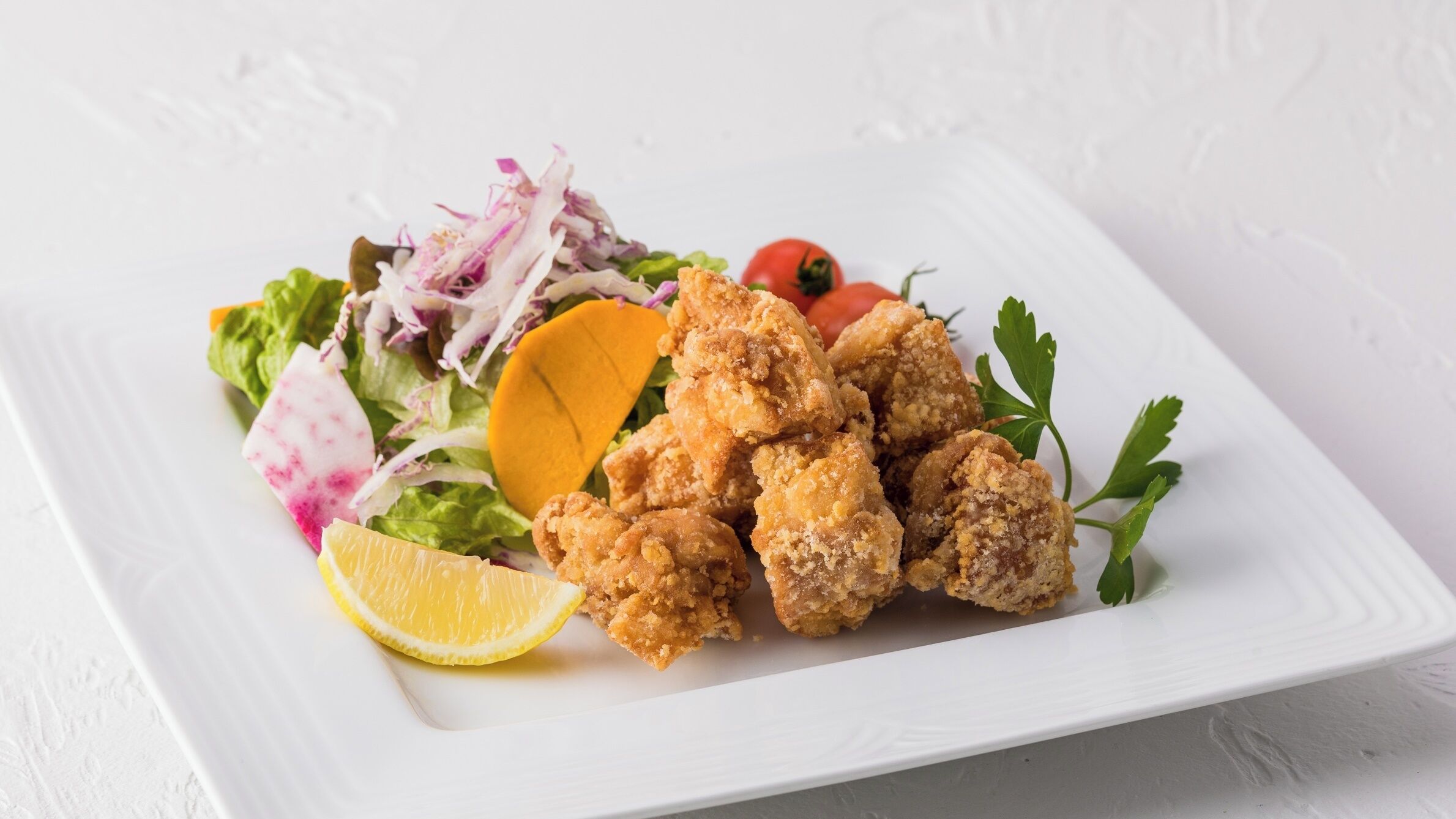 A plate of fried chicken with a side salad, lemon wedge, and cherry tomatoes.