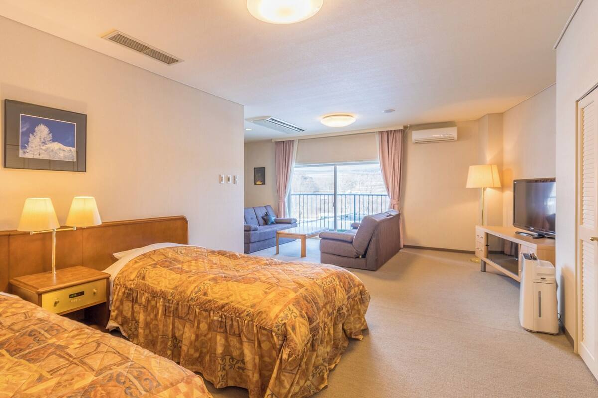 Een hotelkamer met twee bedden, een bank, een televisie en een balkon met gordijnen.