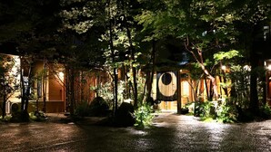 A traditional Japanese-style building with a wooden exterior, a covered entrance, and a gravel pathway leading to the entrance. - Tsumikusa no Yado Komatsu (Kirishima)