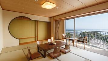 Um quarto japonês tradicional com tatames, uma mesa de madeira baixa e vista para o mar.