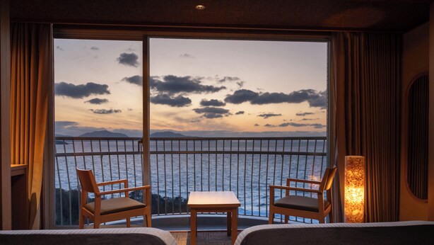 A hotel room with a balcony overlooking a body of water and mountains during sunset. - KAMENOI HOTEL GENKAINADA All-Inclusive Hotel (Kitakyushu)