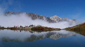 A mountain landscape with a lake reflecting the scenery, a group of people on a rocky outcrop, and mist over the mountains. - Hakuba Happo Onsen Hakuba Marukin Ryokan (Hakuba)