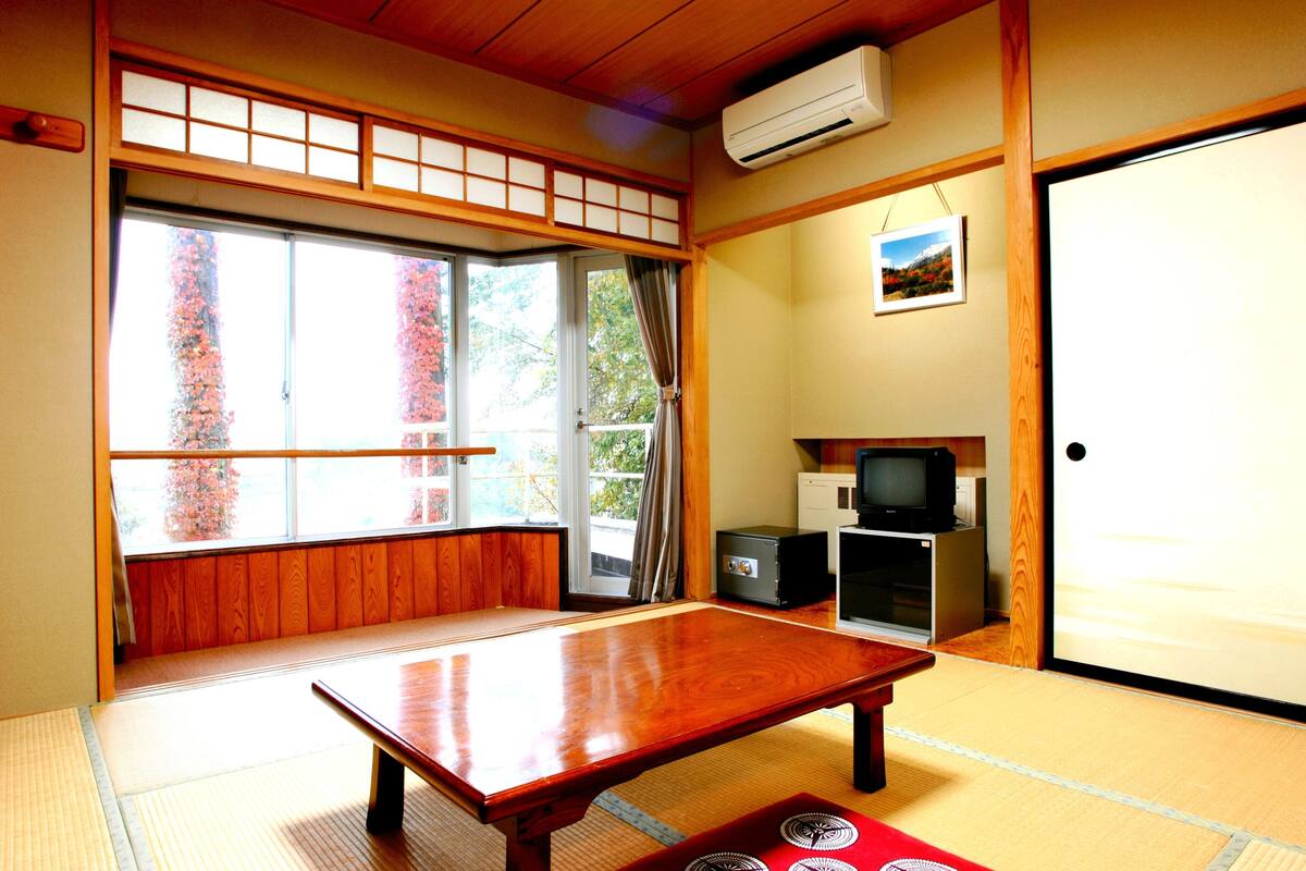 Ein traditioneller japanischer Raum mit Tatami-Boden, einem niedrigen Holztisch, Schiebetüren, einem Fernseher und einem kleinen Kühlschrank.