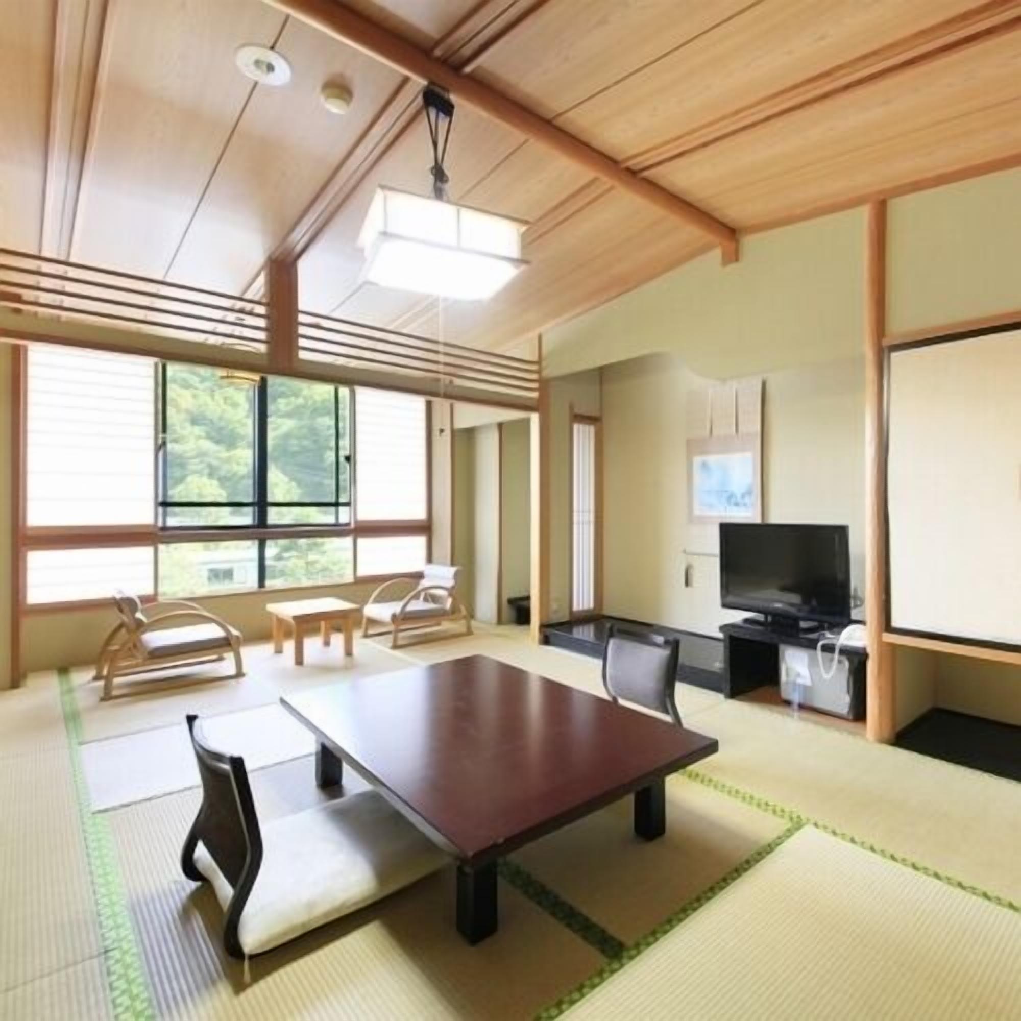 Una habitación tradicional japonesa con suelo de tatami, una mesa baja, sillas, un televisor y una puerta corredera.
