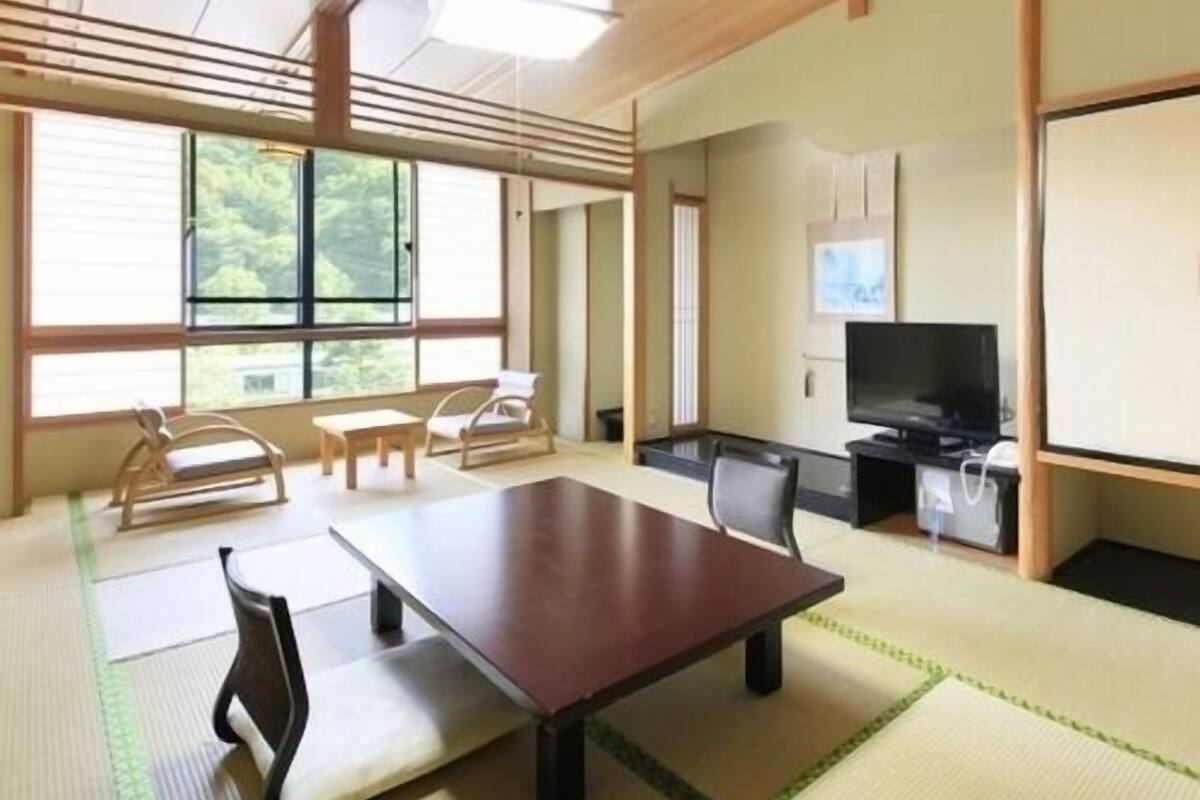 A traditional Japanese-style room with tatami flooring, a low table, chairs, a television, and a sliding door.
