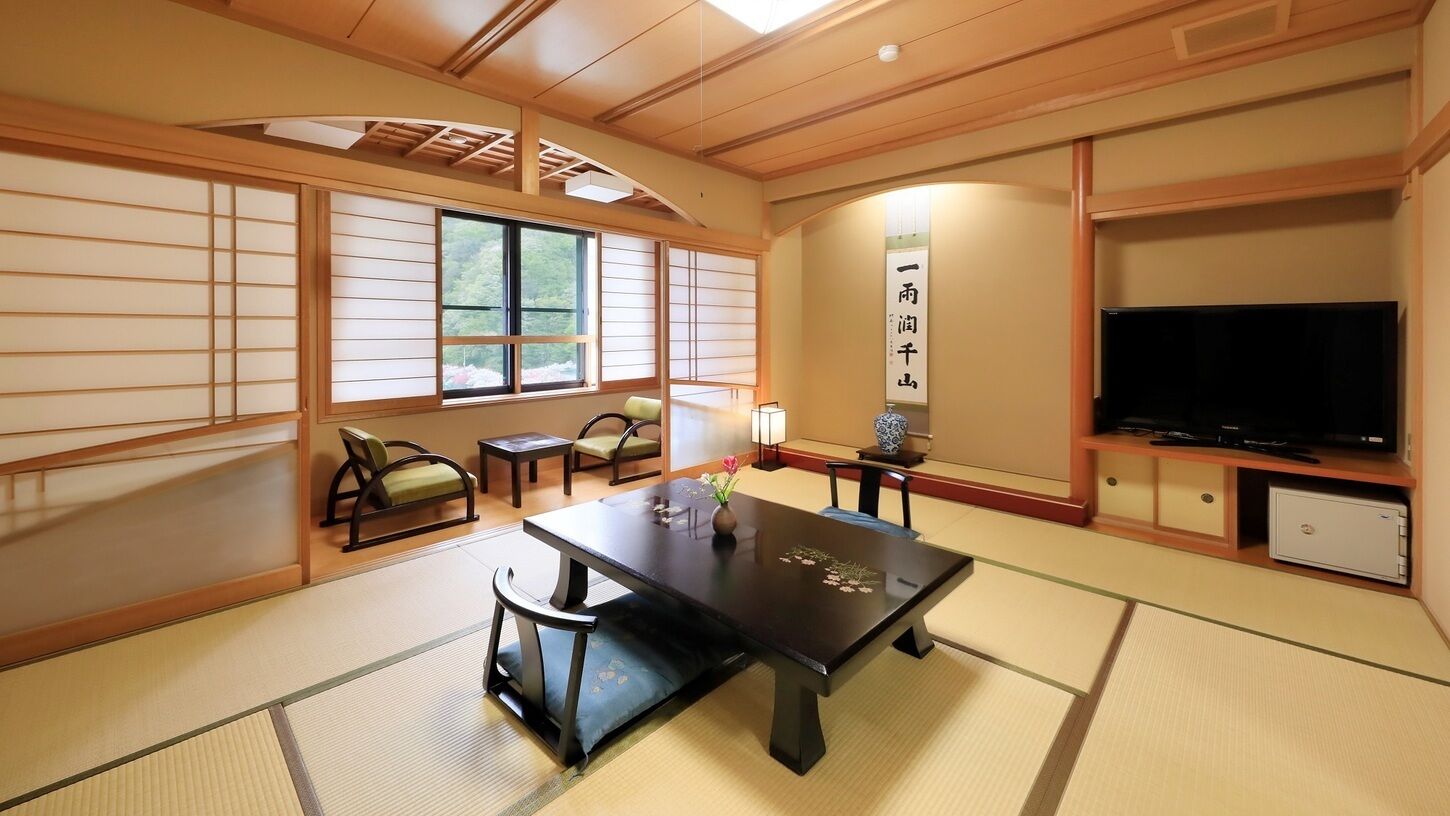 Una habitación japonesa tradicional con suelo de tatami, una mesa baja con cojines, un televisor y un armario.