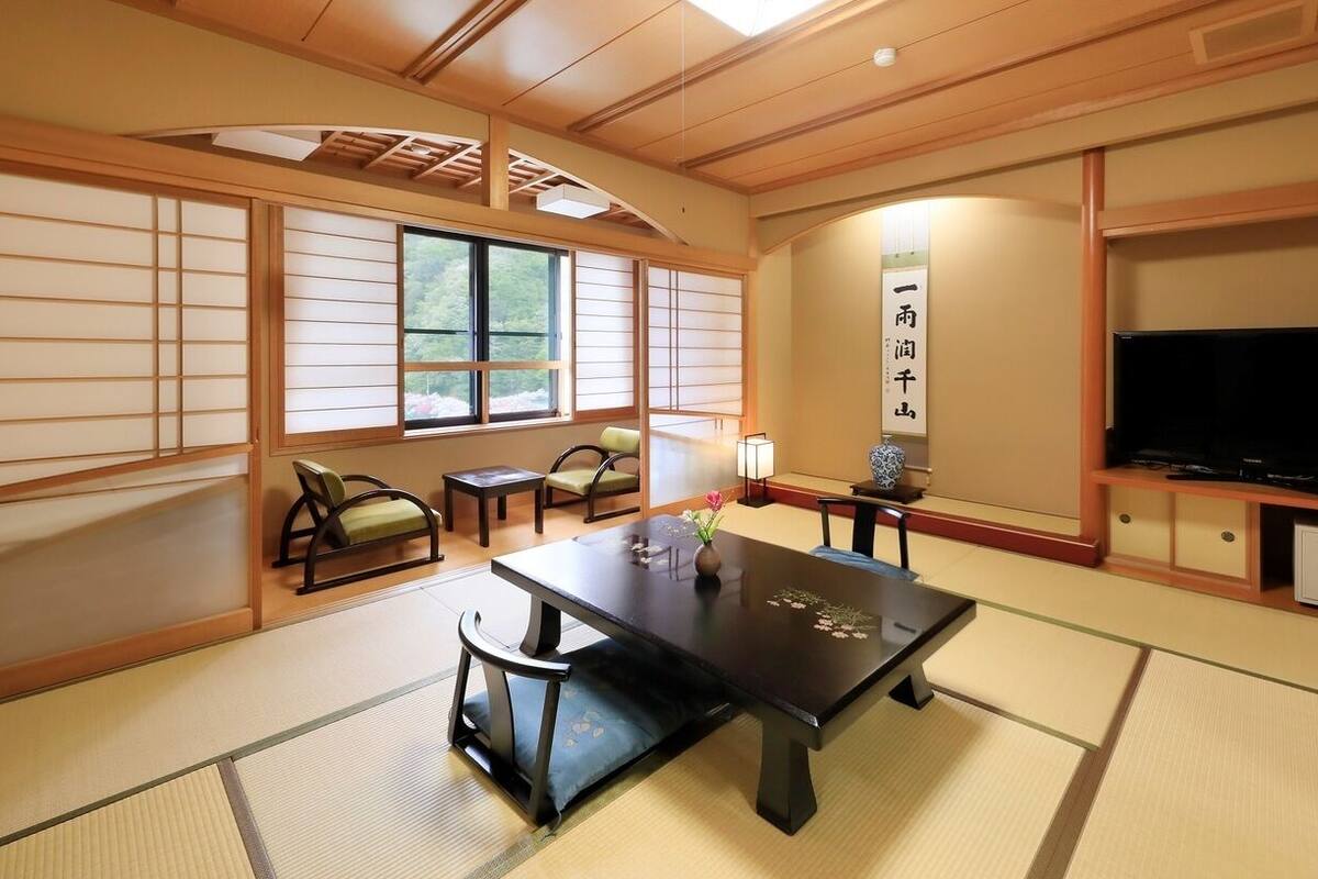 A traditional Japanese room with tatami flooring, a low table with cushions, a television, and a cabinet.