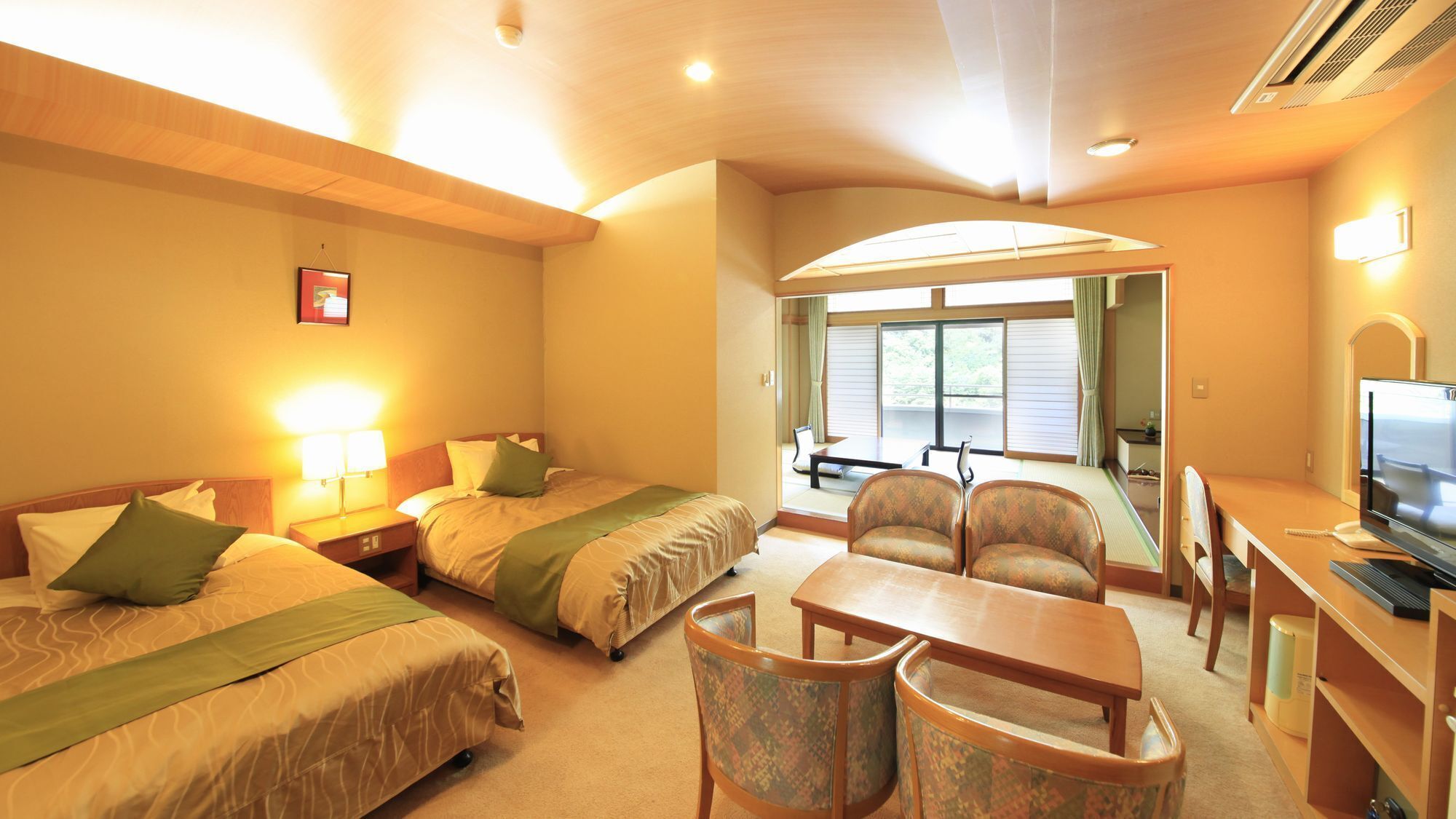 Habitación de hotel con dos camas, un escritorio con computadora, una silla y vista al exterior.