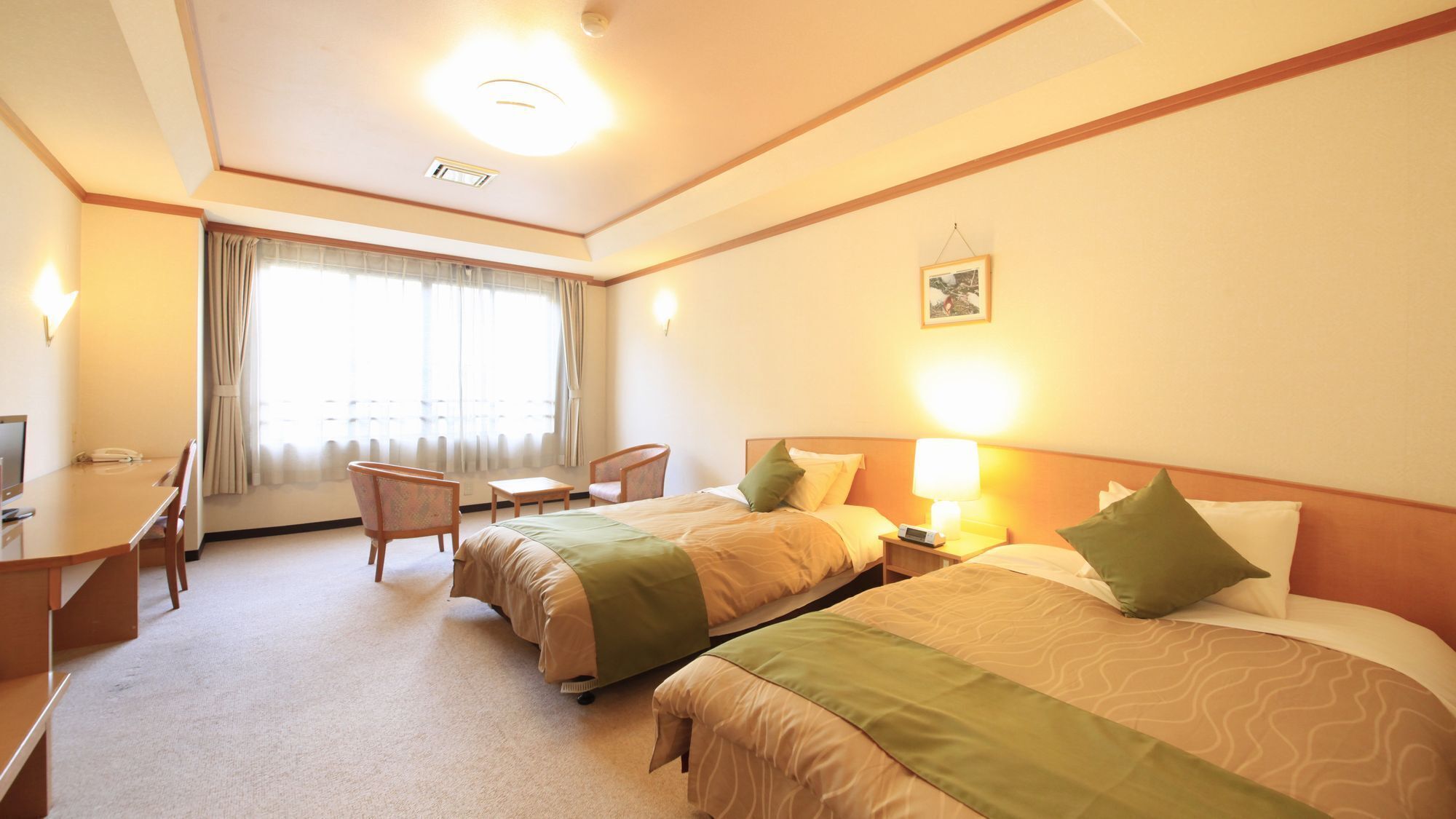 A hotel room with two beds, a desk, a chair, a lamp, and a window with curtains.