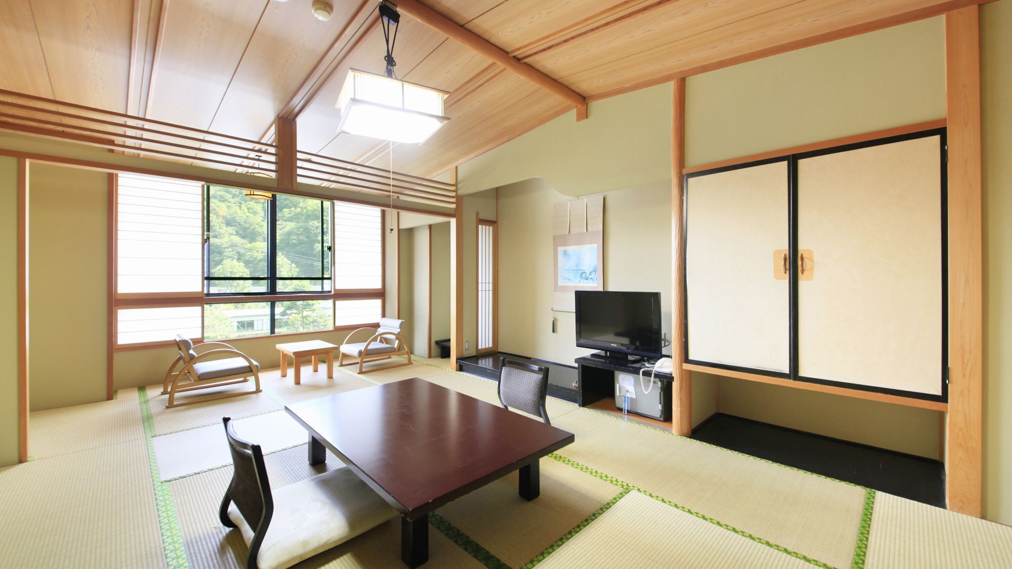 A traditional Japanese room with tatami flooring, a low table, chairs, a television, and sliding doors.