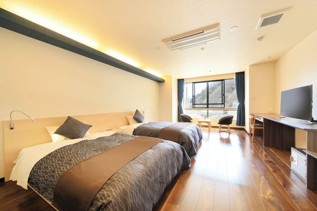A hotel room with two beds, a desk, a TV, and a window with a view.
