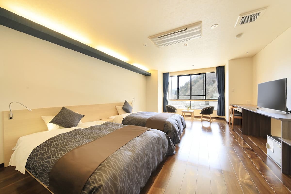 A hotel room with two beds, a desk, a TV, and a window with a view.