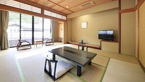 A traditional Japanese-style room with tatami flooring, a low table, a sofa, and a television. - Hotel Achigawa (Achi)