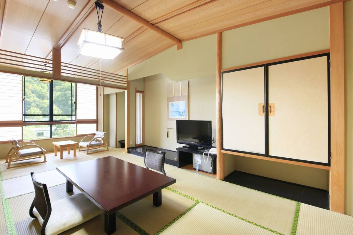 A traditional Japanese room with tatami flooring, a low table, chairs, a television, and sliding doors.