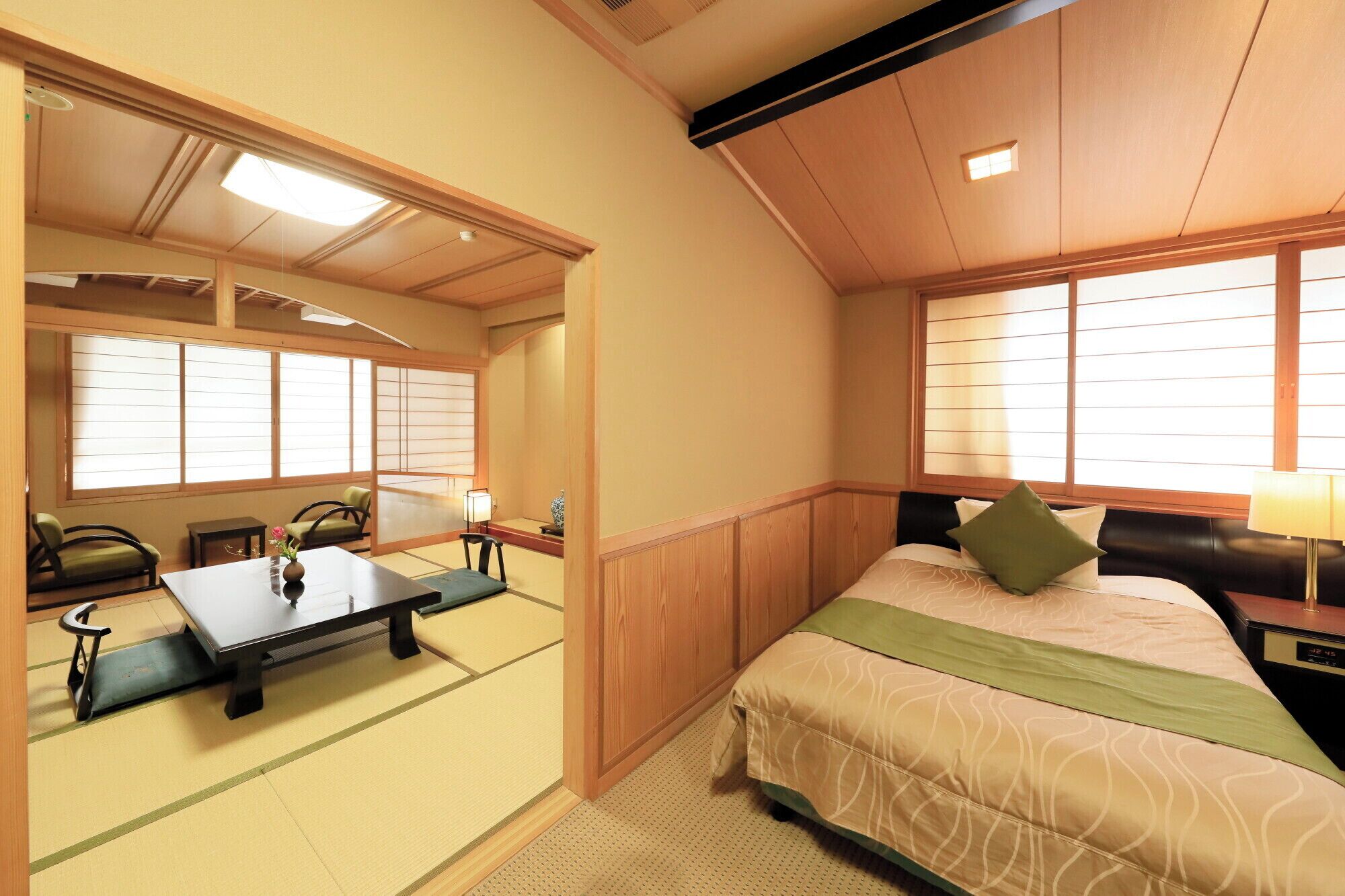 Una habitación tradicional japonesa con suelo de tatami, una mesa baja, una cama con almohada verde y puertas correderas shoji.