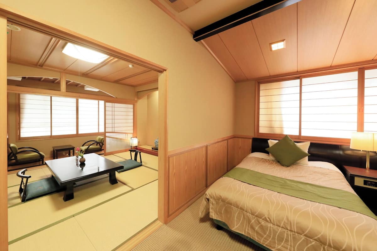 A traditional Japanese-style room with tatami flooring, a low table, a bed with a green pillow, and sliding shoji doors.