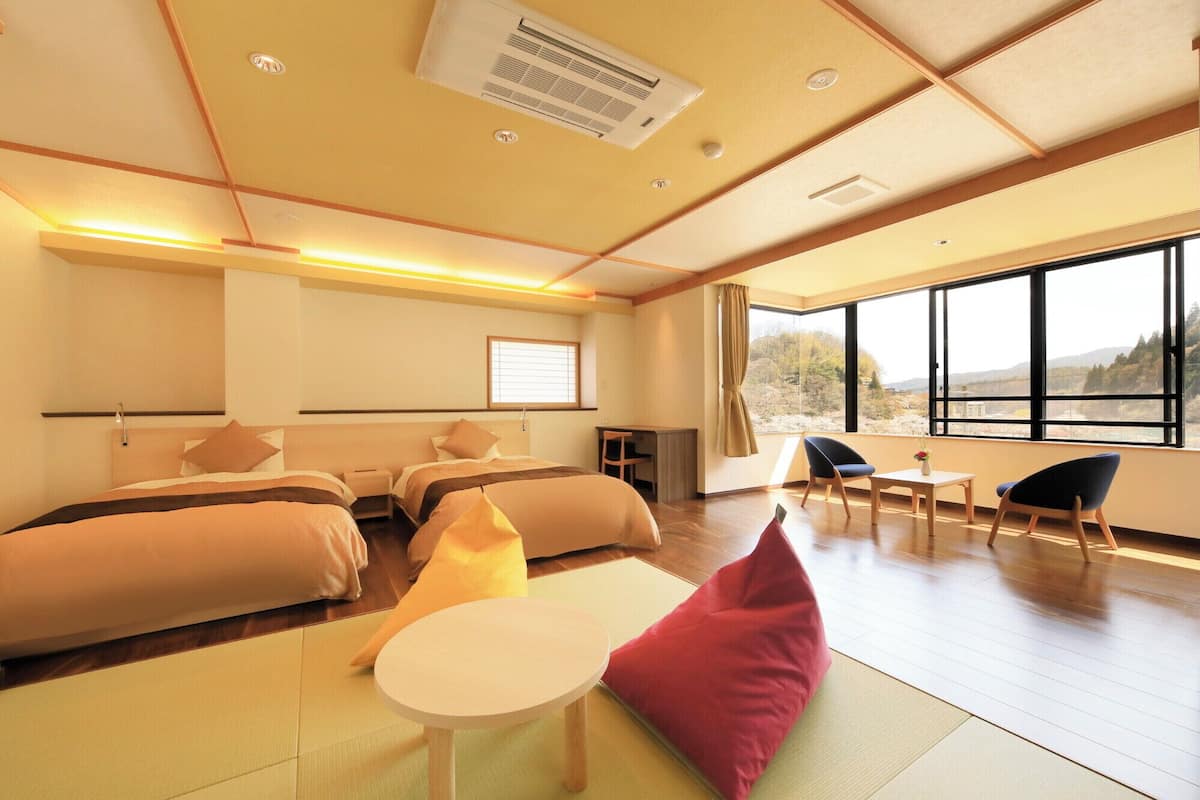 A hotel room with a bed, a desk, a chair, a small table, and a large window offering a view.