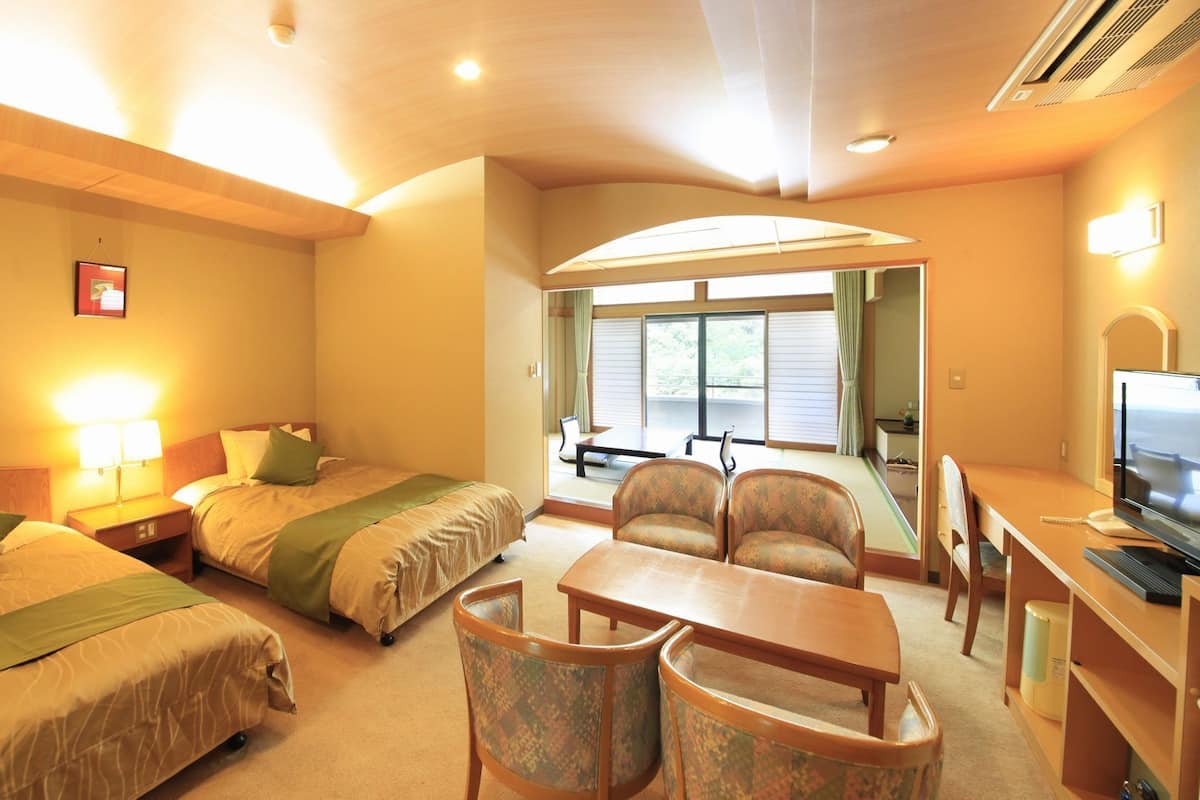 A hotel room with two beds, a desk with a computer, a chair, and a view of the outdoors through a large window.