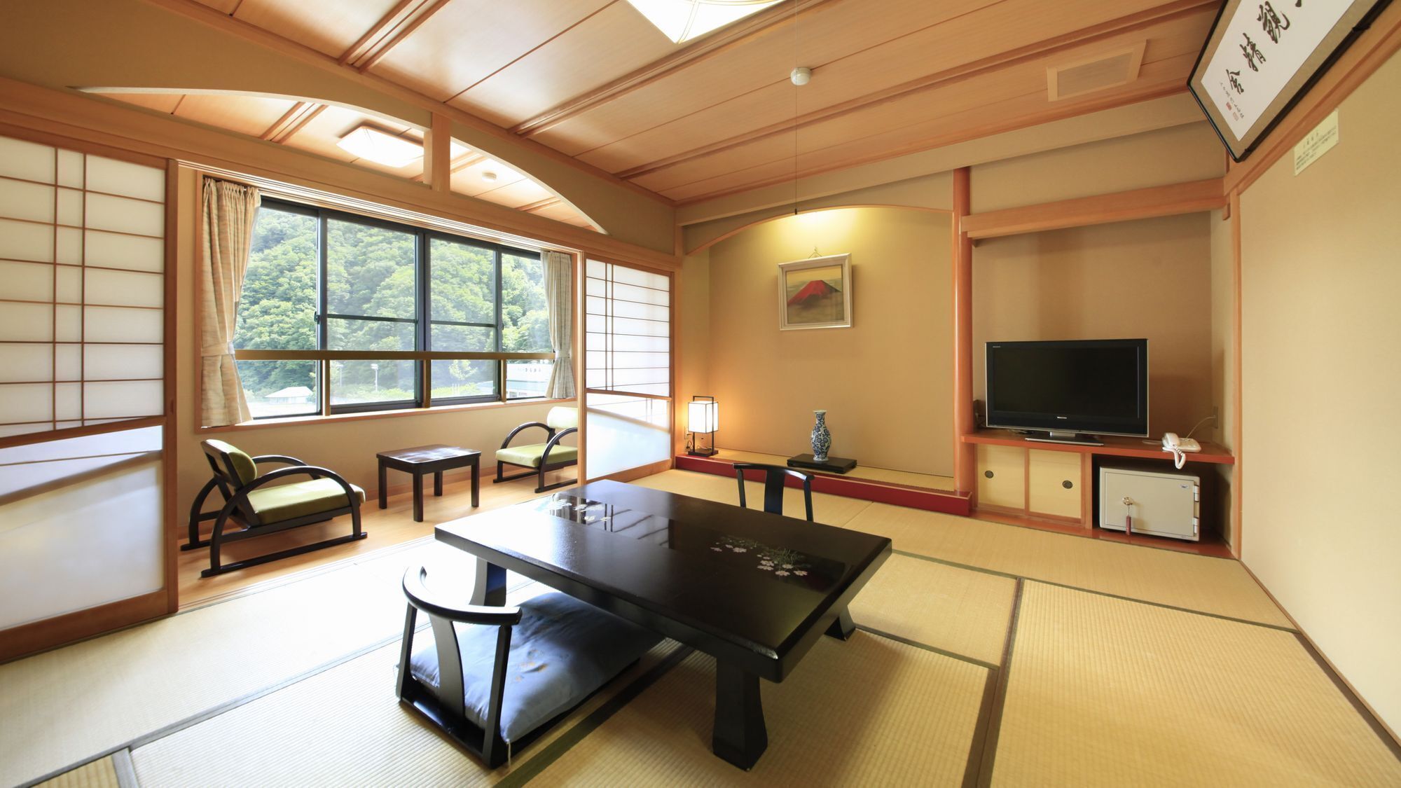 Una habitación japonesa tradicional con suelo de tatami, una mesa baja, un sofá, un televisor y una ventana con vistas a zonas verdes.