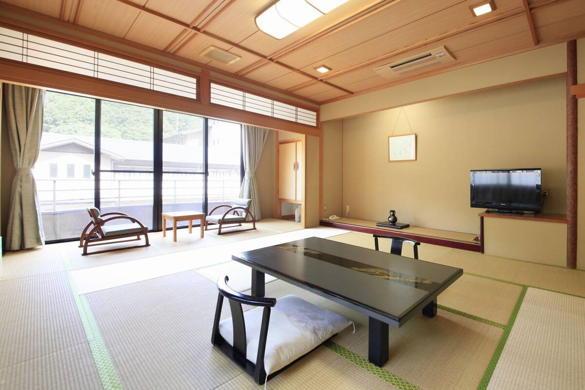 A tatami mat room with a tatami mat table, a television, and a view of a building outside.