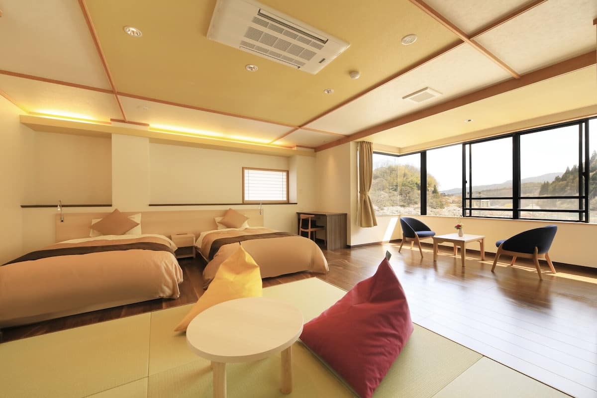 A hotel room with two beds, a desk, a chair, a small table, and large windows with a view.