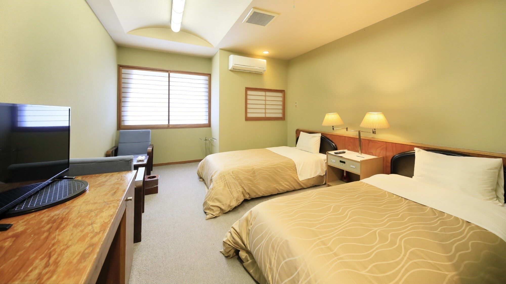 A hotel room with two beds, a desk with a computer, a chair, and a window with blinds.