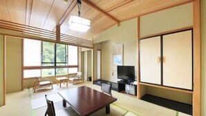 A traditional Japanese room with tatami flooring, a low table, a sofa, and a television. - Hotel Achigawa (Achi)