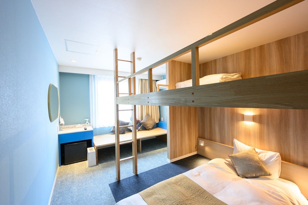 Une chambre avec un lit superposé, un bureau et une chaise, une échelle et une table de chevet avec une lampe.
