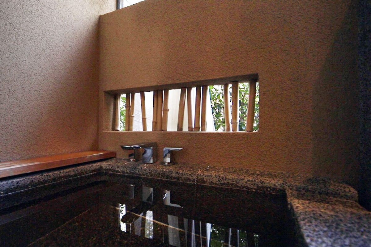A bathroom with a granite countertop, a mirror, and a window with vertical blinds.