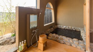 Un baño con suelo de madera, una bañera de piedra, un banco de madera y una ventana con vistas.