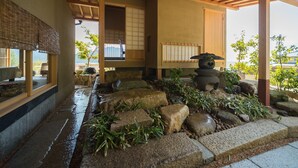 Una habitación tradicional japonesa con suelo de tatami, una fuente de agua de piedra y vista al mar.