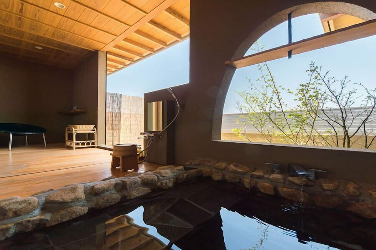 A modern interior with a stone-lined pool, wooden flooring, and a large window offering a view of the outdoors.