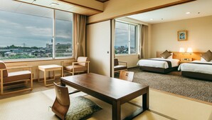 Hotelkamer met een groot raam, een houten tafel, twee bedden en uitzicht op de stad.