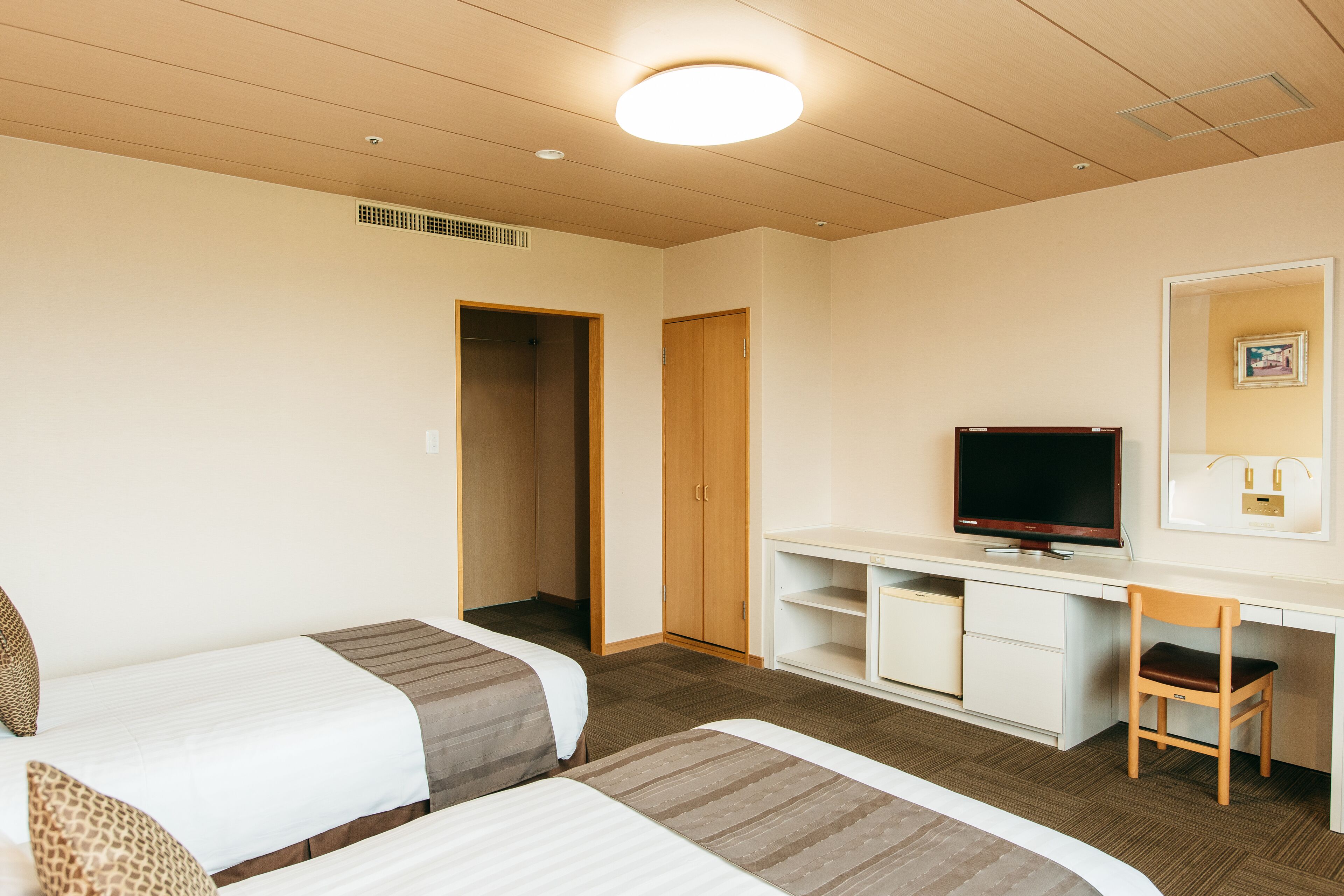 Habitación de hotel con dos camas, un escritorio con televisor, una silla y un armario.