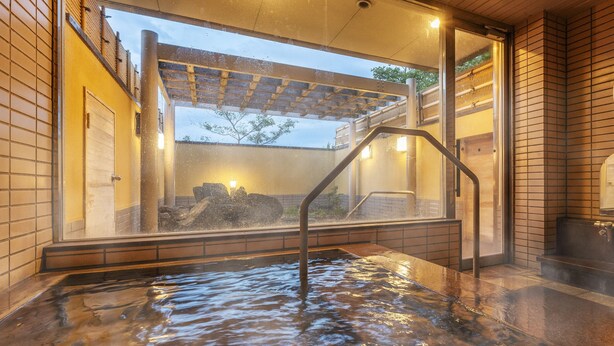 Een warmwaterbrongebied met een houten pergola, een stenen muur en uitzicht op een gebouw met een balkon.