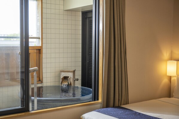 Una habitación de hotel con una cama, un ventanal con vistas a una piscina y un taburete de madera cerca de la ventana.