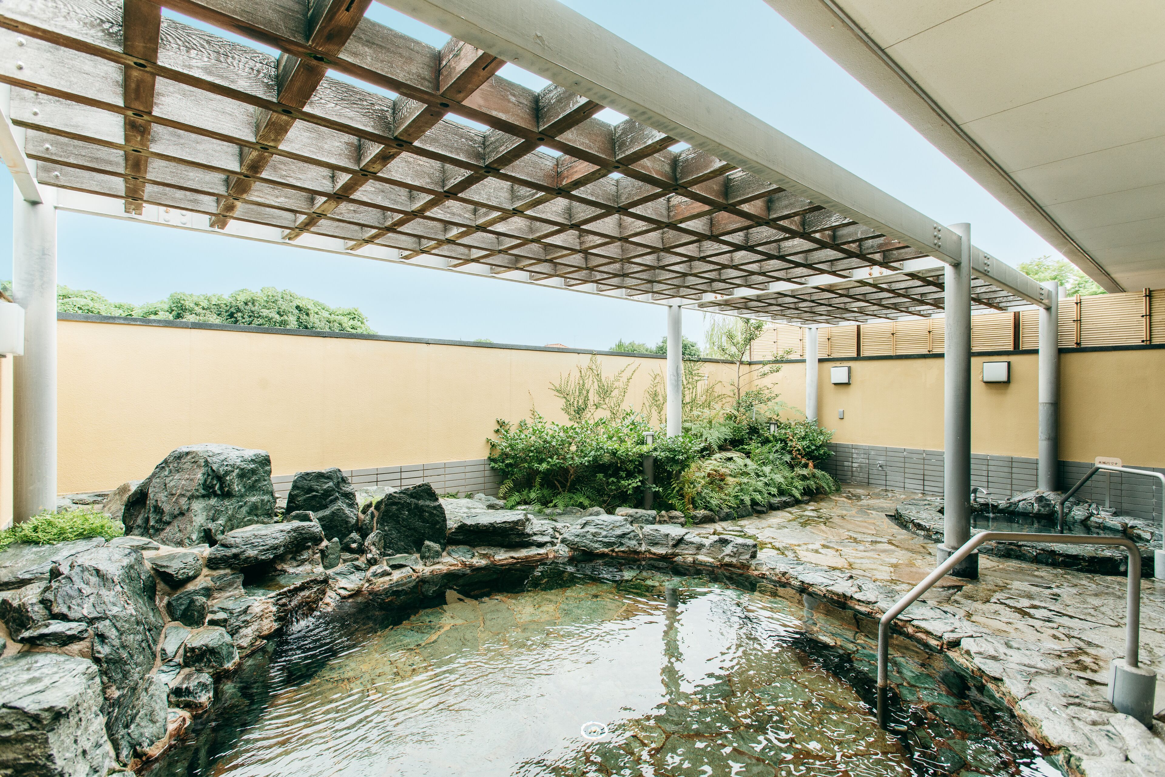A covered outdoor area with a stone water feature, a wooden pergola, and a yellow wall.