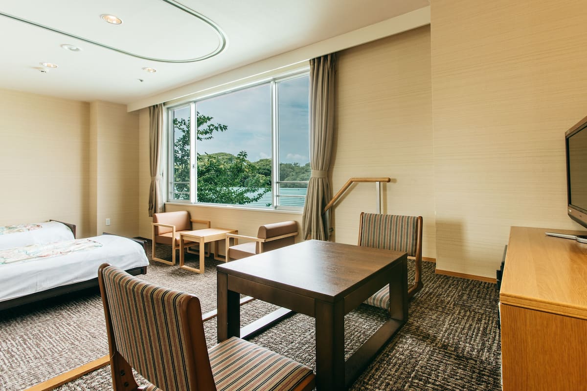 A hotel room with a bed, a desk, a chair, a small table, and a television.