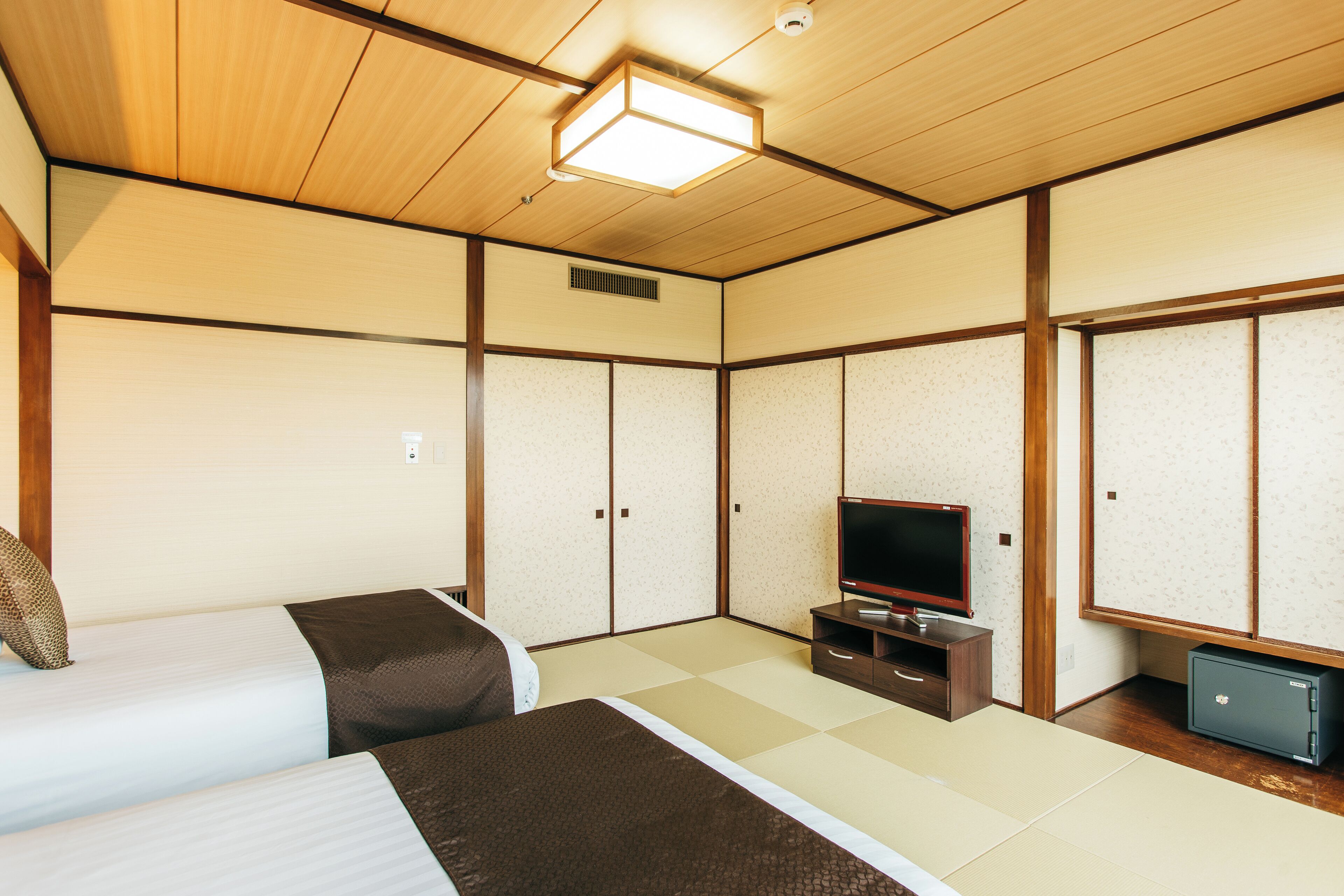 A traditional Japanese room with tatami flooring, a television on a wooden stand, and two beds with dark and light bedding.