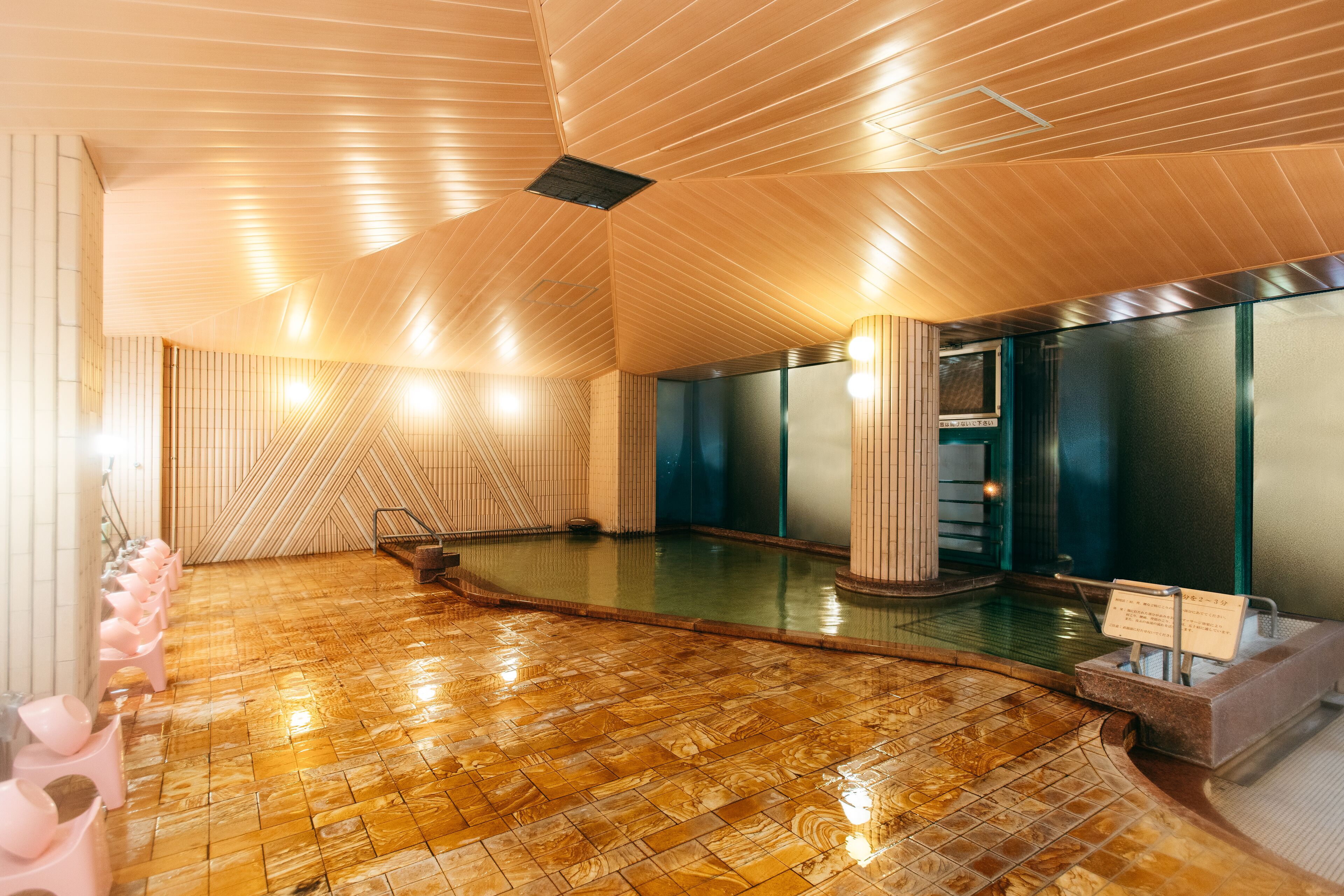 A modern spa with a wooden floor, a central pool, and a row of pink chairs.